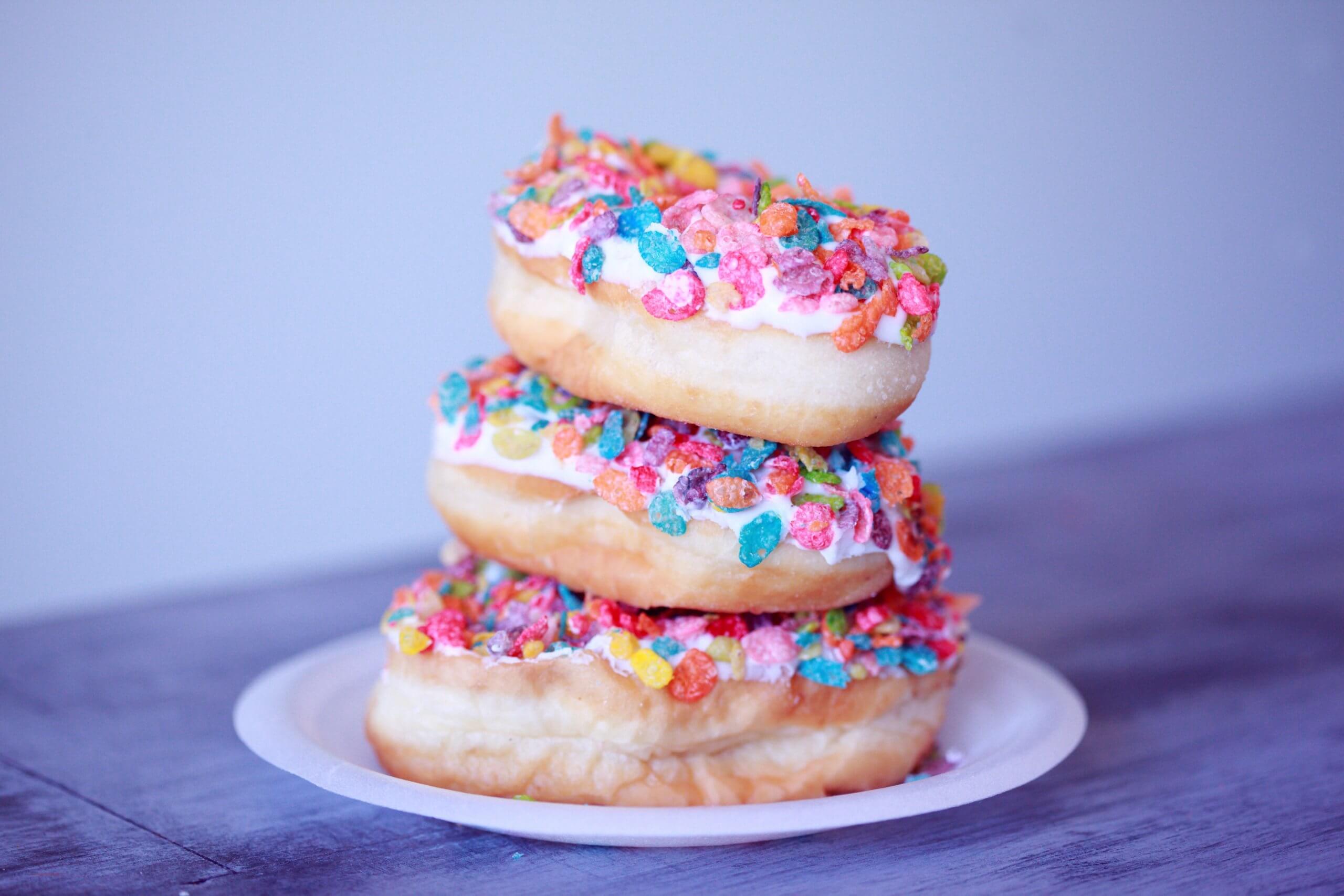 Bunte Donuts sind übereinander gestapelt auf einer lila farbenden Tischdecke